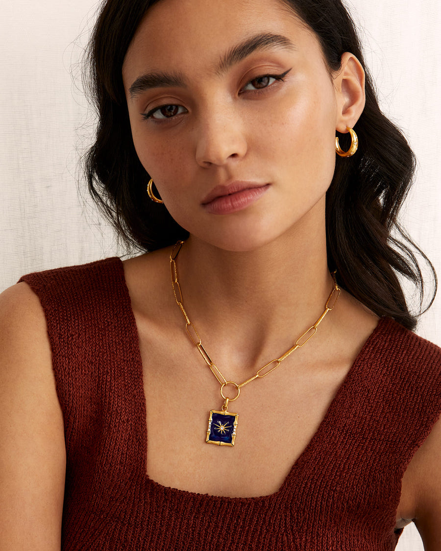 SORU SMALL GOLD HOOP EARRING WITH CLEAR CRYSAL STARS ETCHED INTO THE GOLD PLATED SILVER AND BLUE ENAMEL CHARM NECKLACE ON THE MODEL