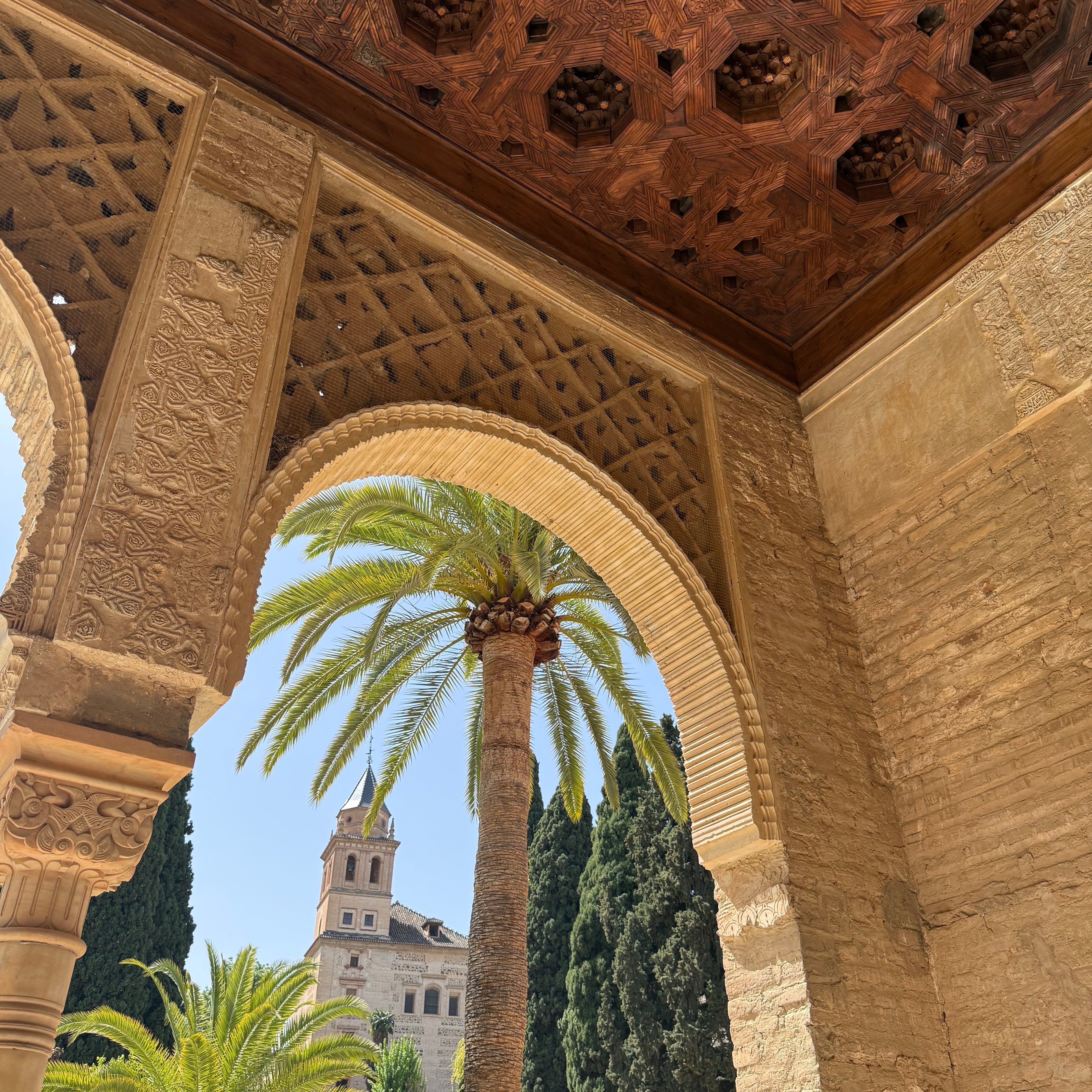 image of an archway in the Alhambra palace with a palm tree and church in the background
