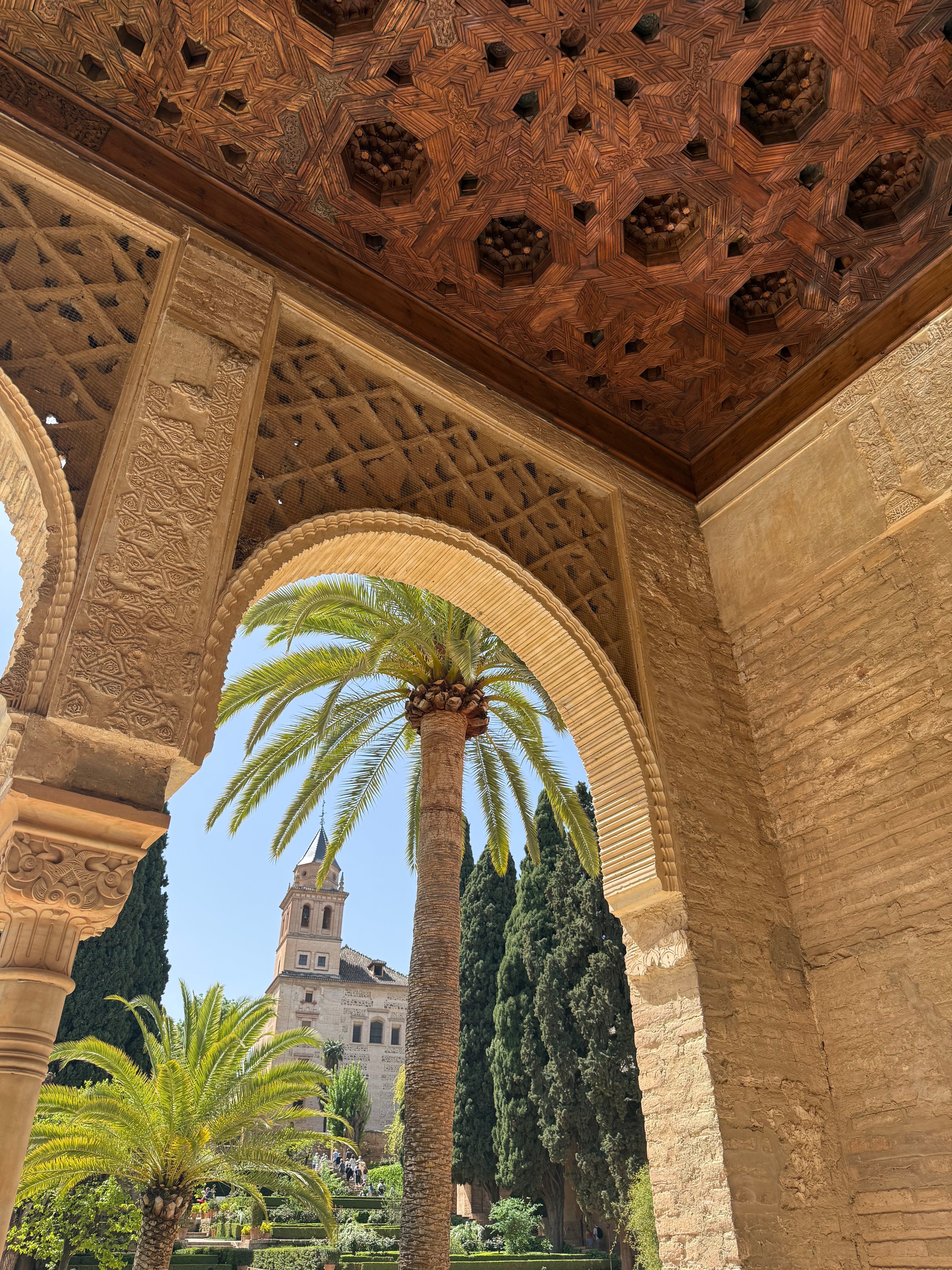 image of an archway in the Alhambra palace with a palm tree and church in the background