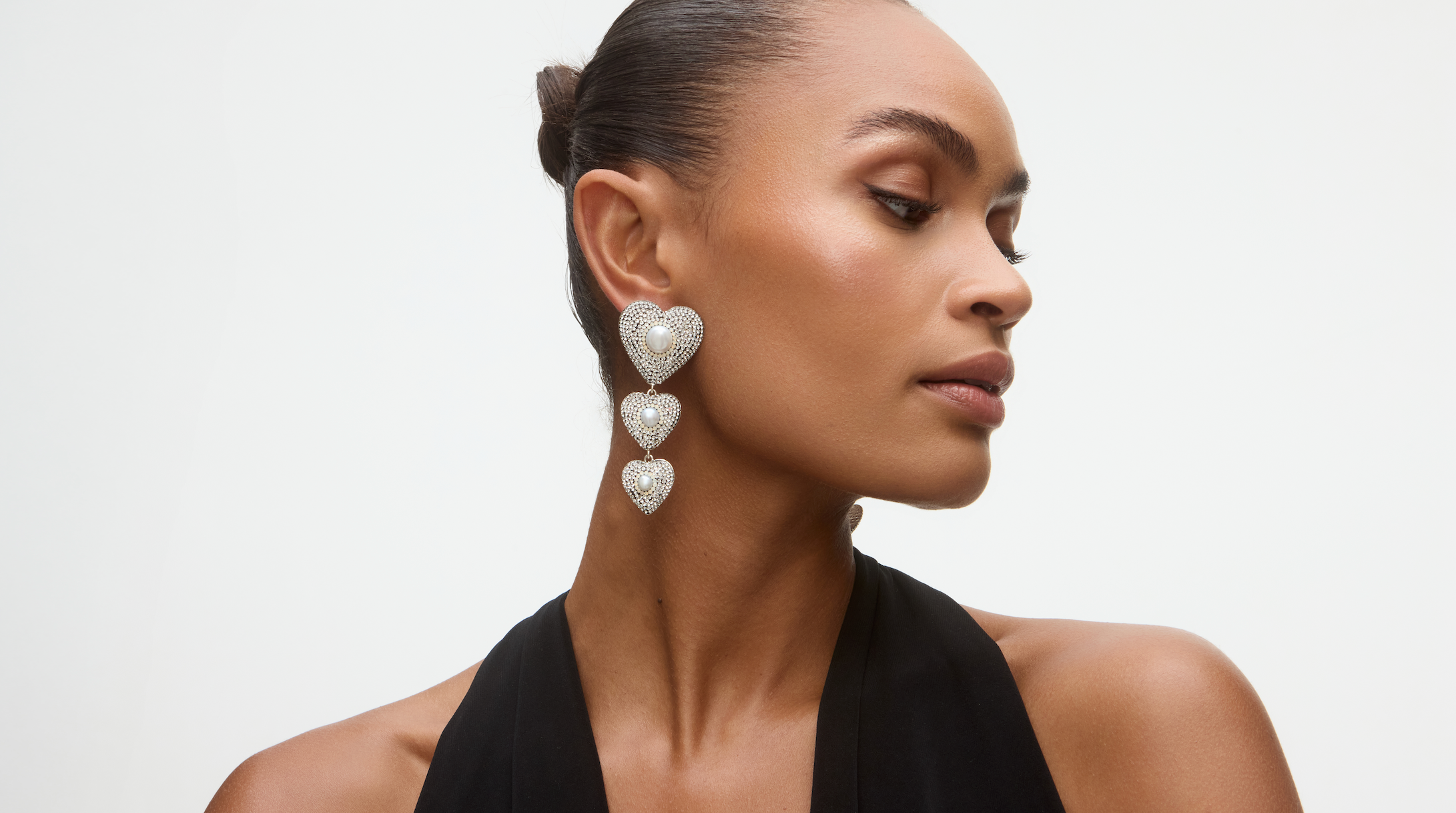 Lady looking to the side with triple heart drop earrings with pearl centre and crystals.