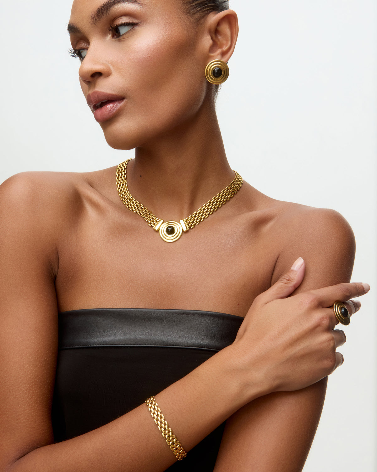 Image of a lady wearing black dress, gold chain bracelet, matching choker with round onyx detail and matching stud earrings.
