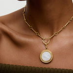 Woman wearing a white and gold charm pendant necklace, with neutral background