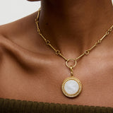 Woman wearing a white and gold charm pendant necklace, with neutral background