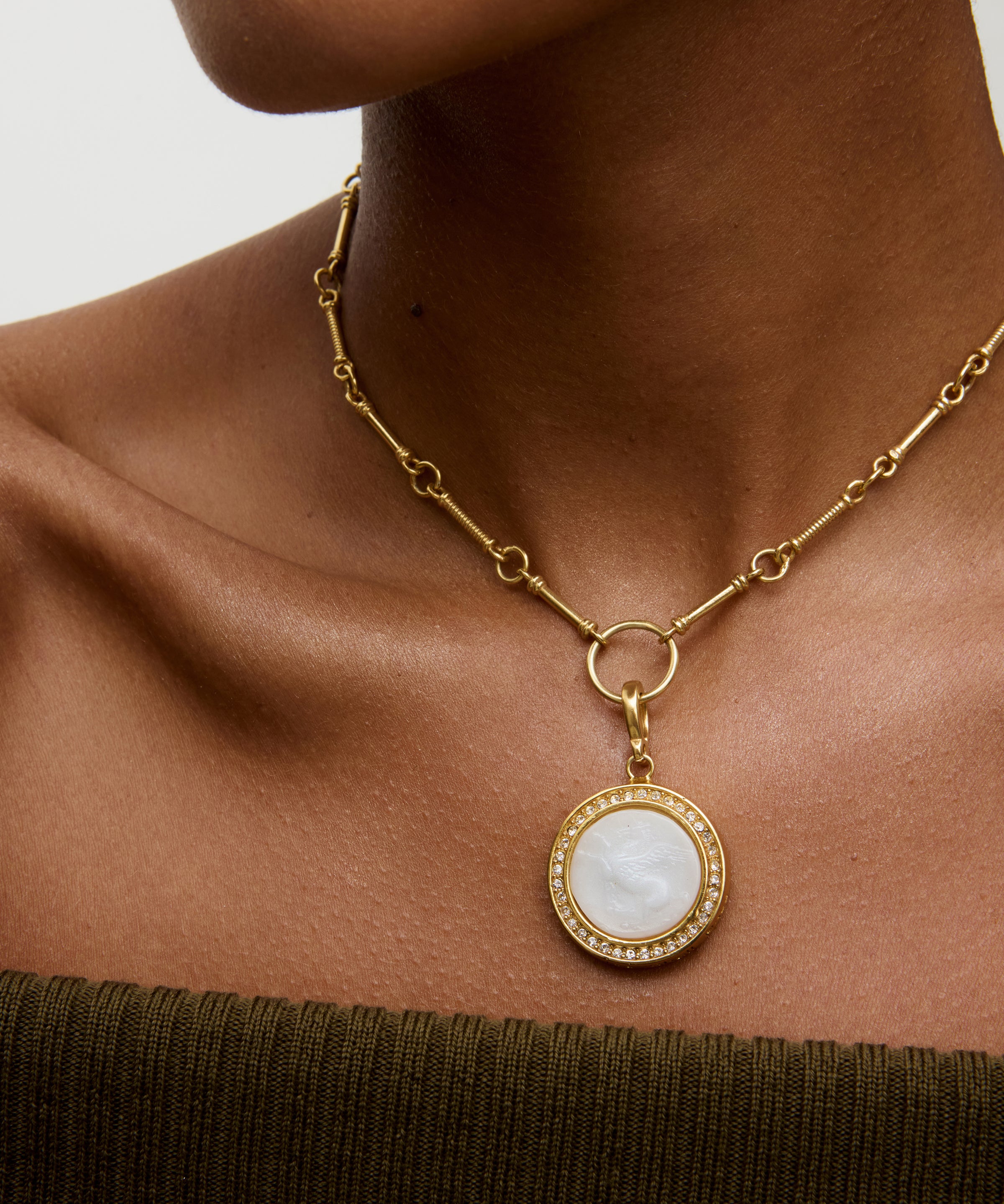 Woman wearing a white and gold charm pendant necklace, with neutral background