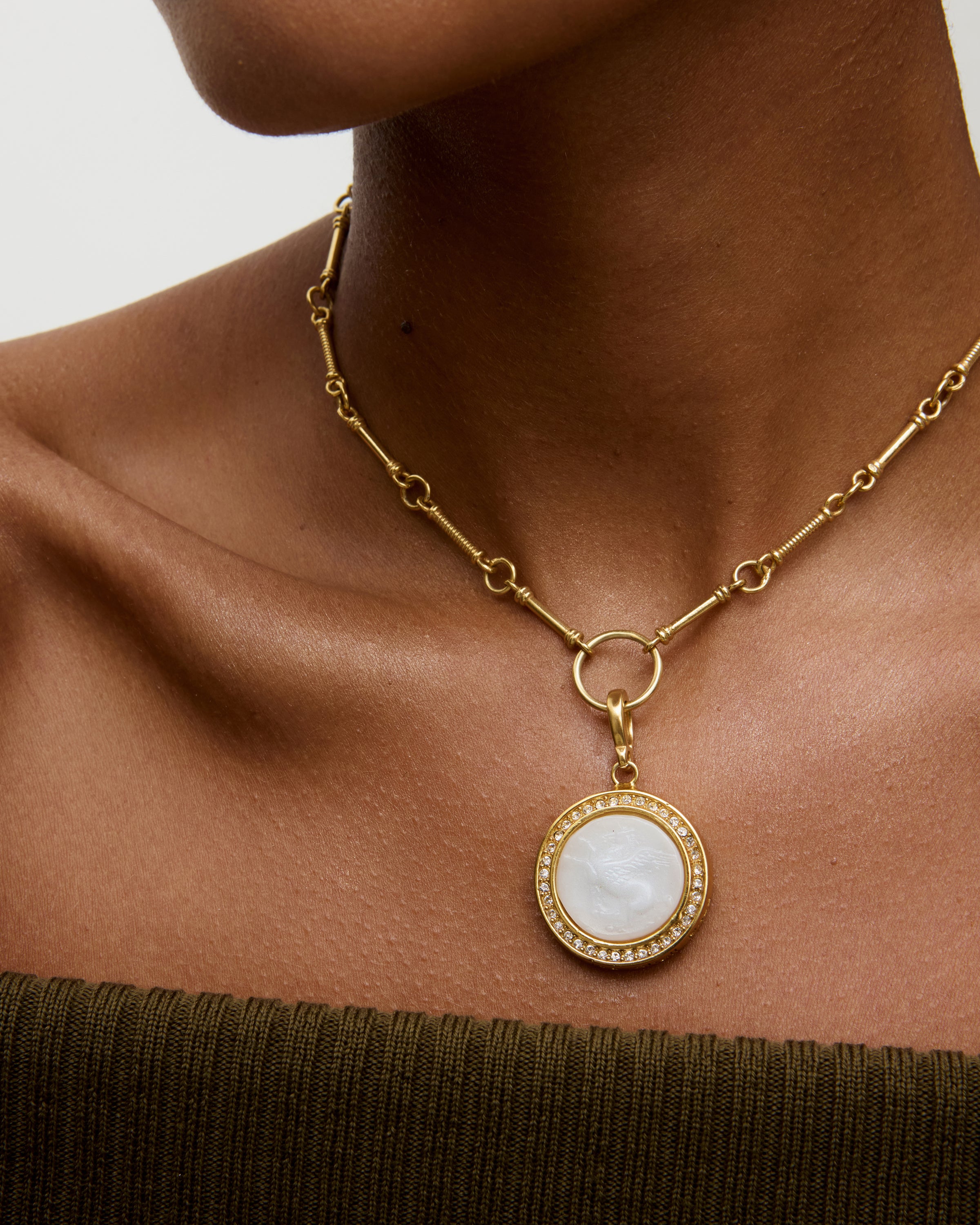 Woman wearing a white and gold charm pendant necklace, with neutral background