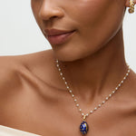 Close-up of a woman wearing a necklace with a blue egg shaped pendant with gold moon and stars on it  on a neutral background