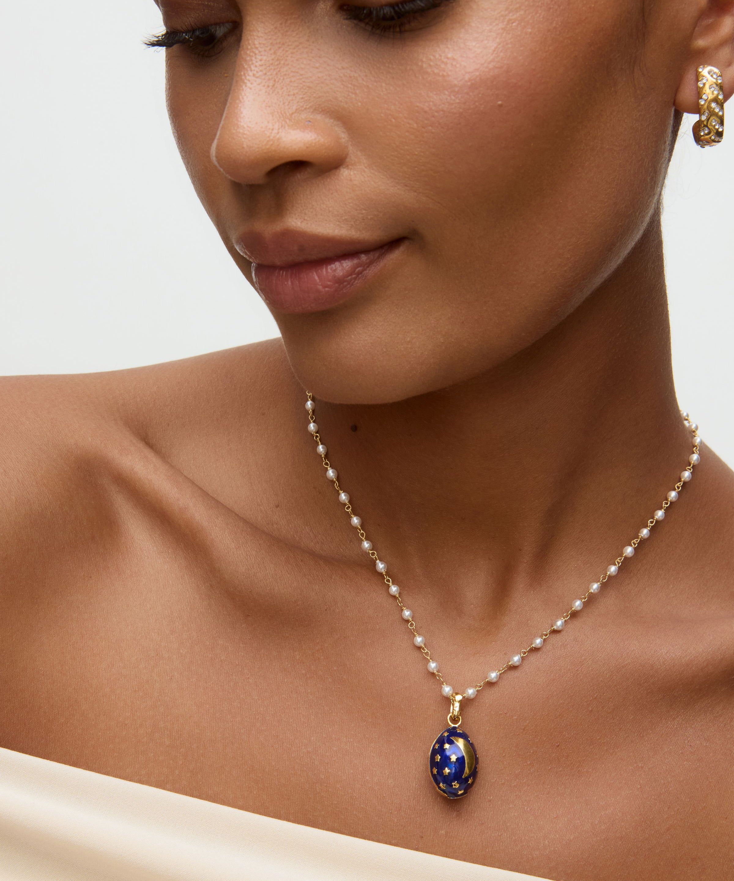 Close-up of a woman wearing a necklace with a blue egg shaped pendant with gold moon and stars on it  on a neutral background