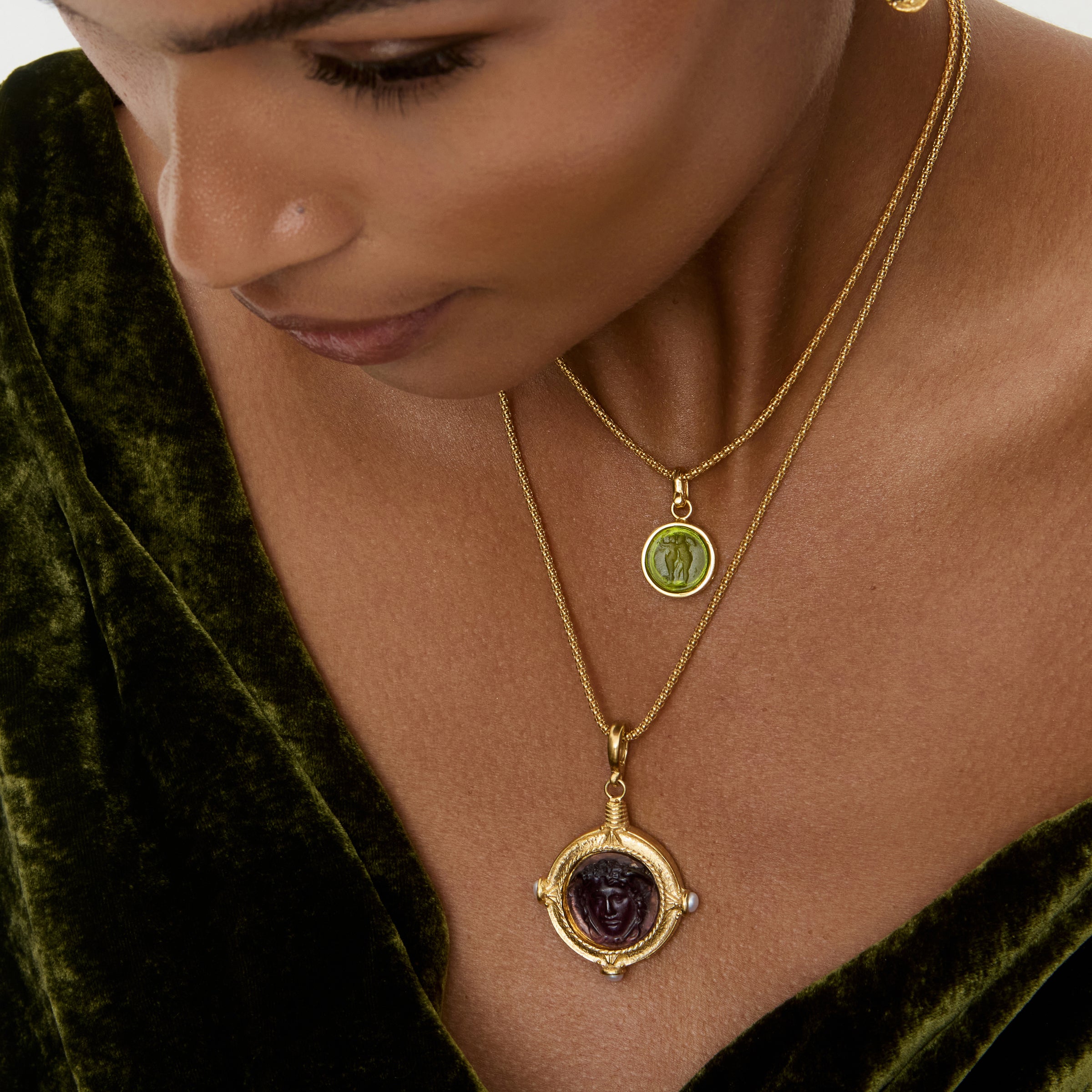 Woman wearing a gold necklace with a pendant, set against a green velvet background.
