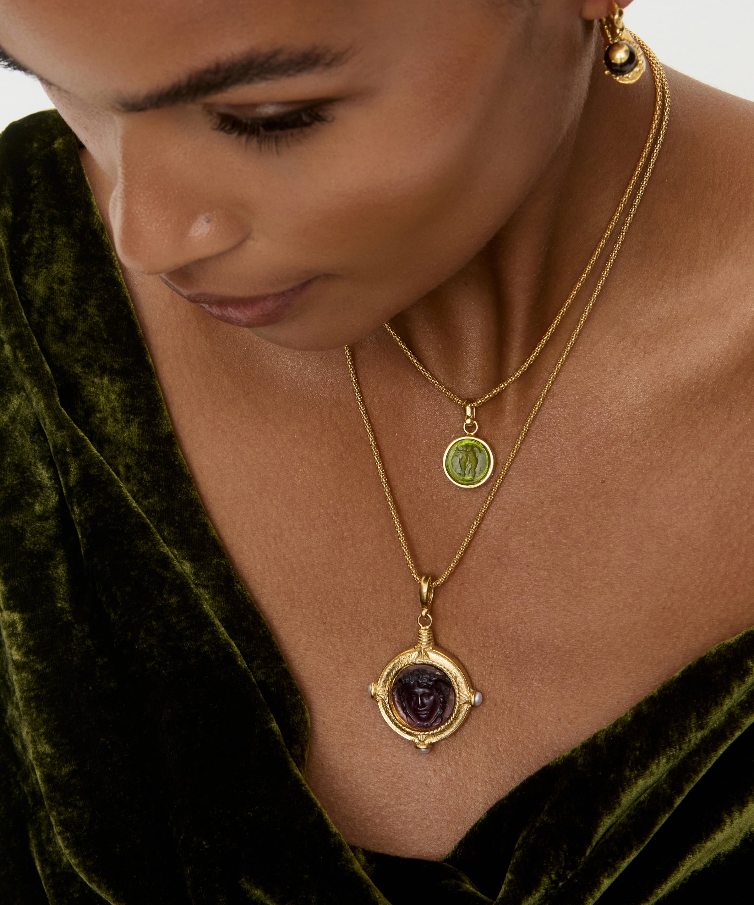 Woman wearing a gold necklace with a pendant, set against a green velvet background.