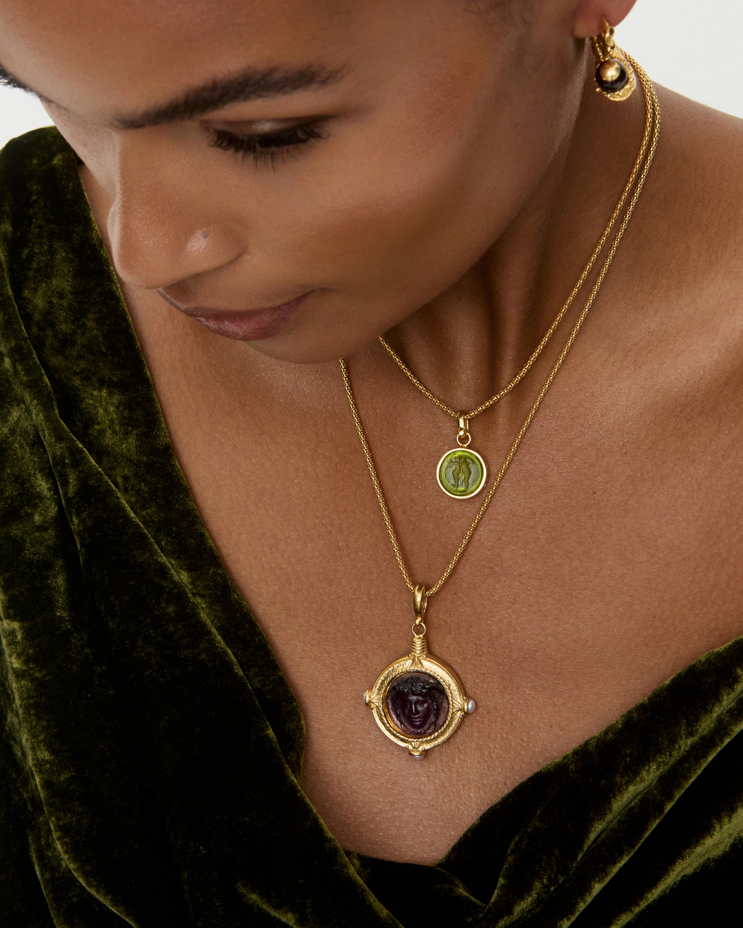 Woman wearing a gold necklace with a pendant, set against a green velvet background.