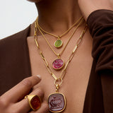 Close-up of a person wearing multiple gold necklaces with gemstone pendants.