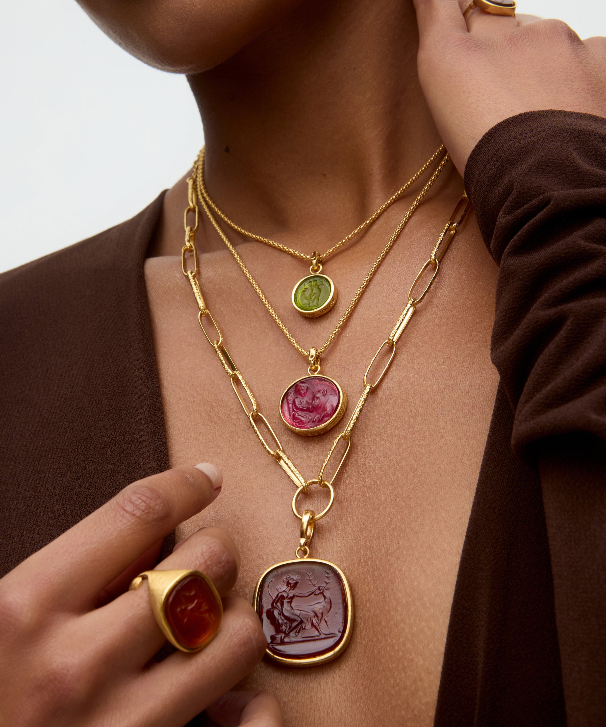 Close-up of a person wearing multiple gold necklaces with gemstone pendants.