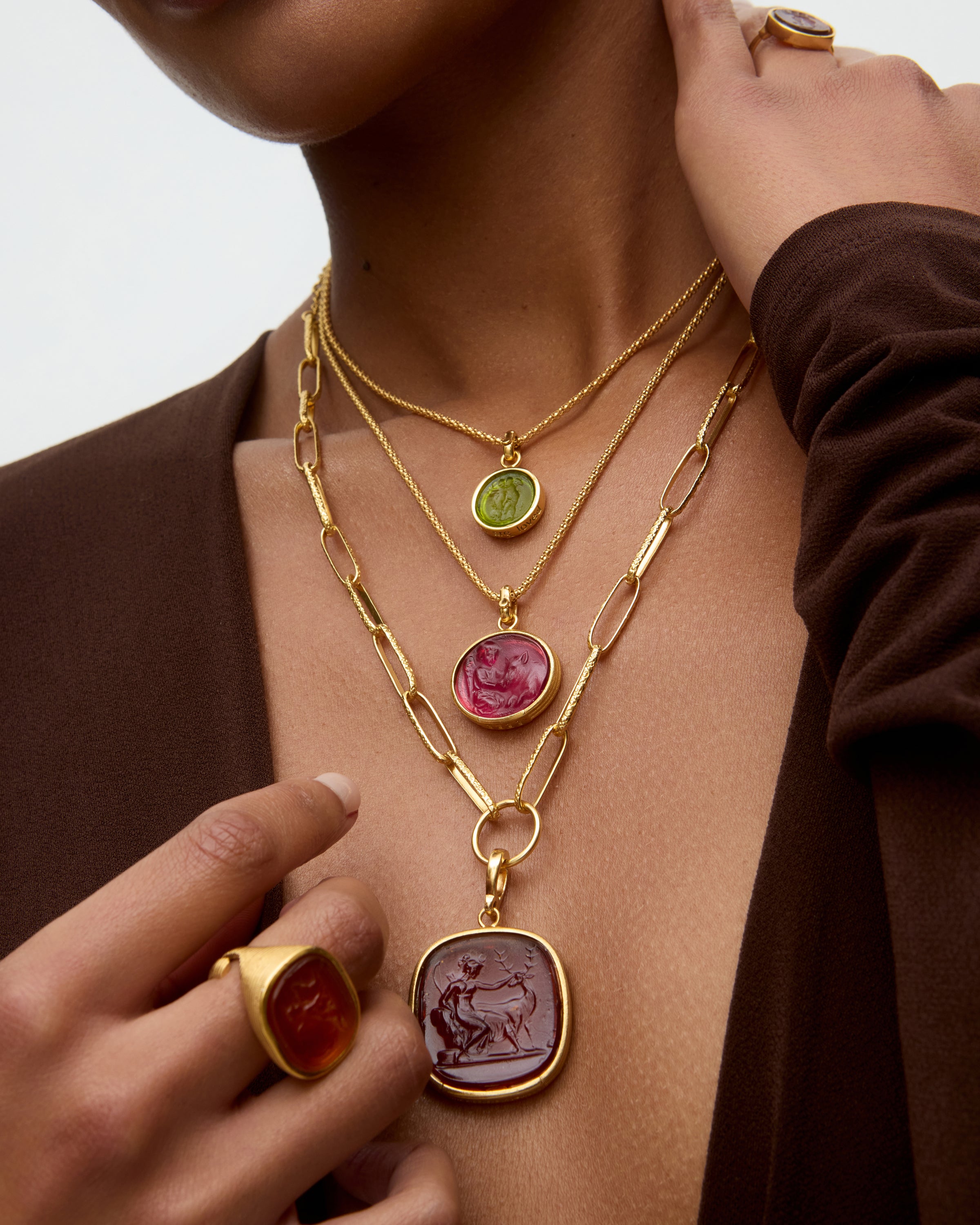 Close-up of a person wearing multiple gold necklaces with gemstone pendants.