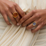 Two hands wearing coloured murano glass rings against a white draped dress