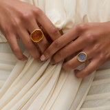Two hands wearing coloured murano glass rings against a white draped dress