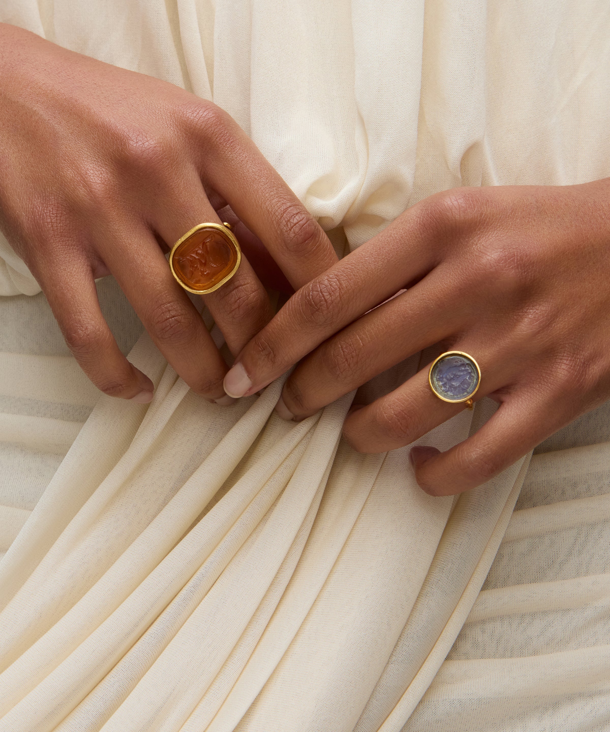 Two hands wearing coloured murano glass rings against a white draped dress