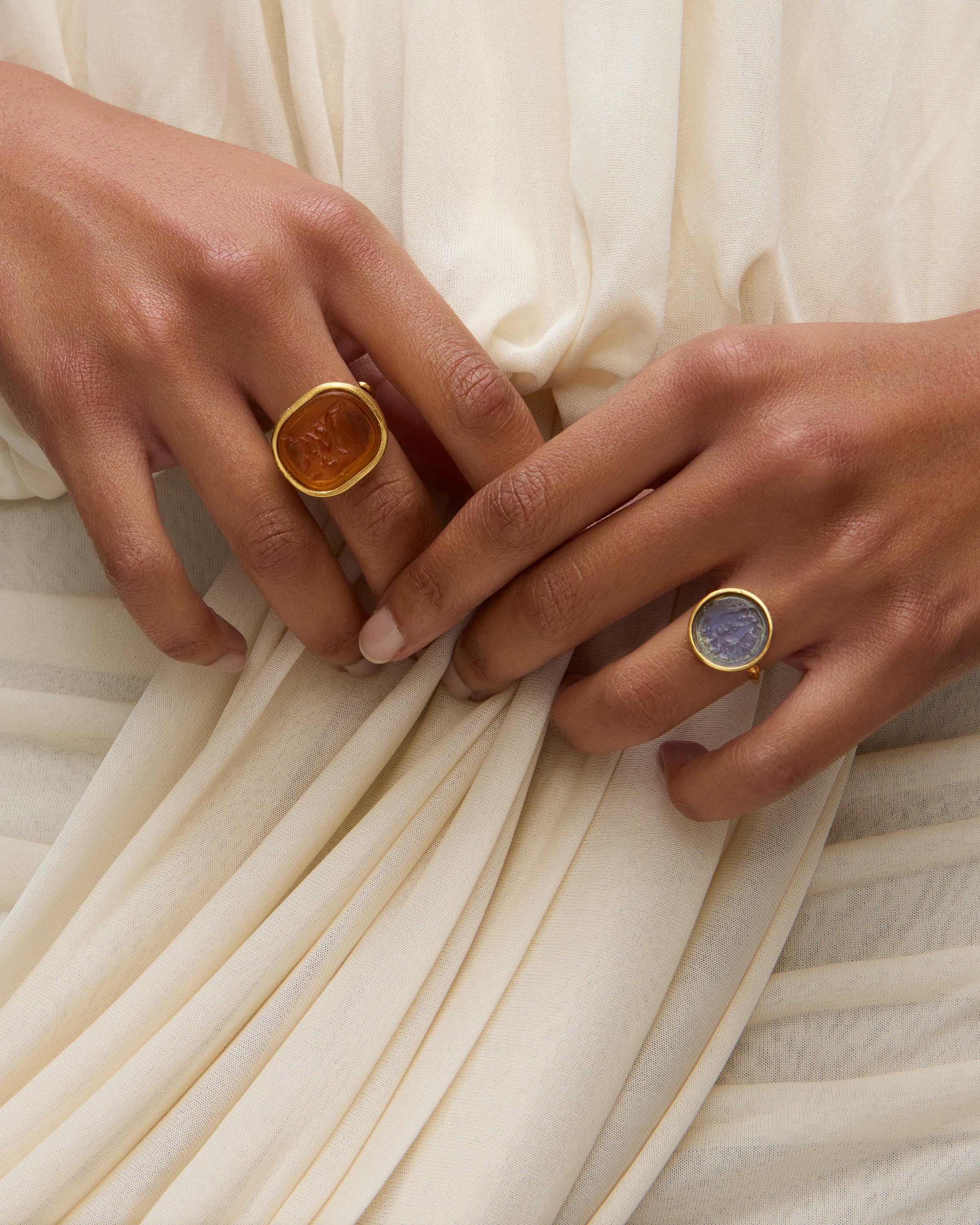 Two hands wearing coloured murano glass rings against a white draped dress