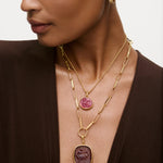 Close-up of a woman wearing a gold necklace with pink and purple pendants.