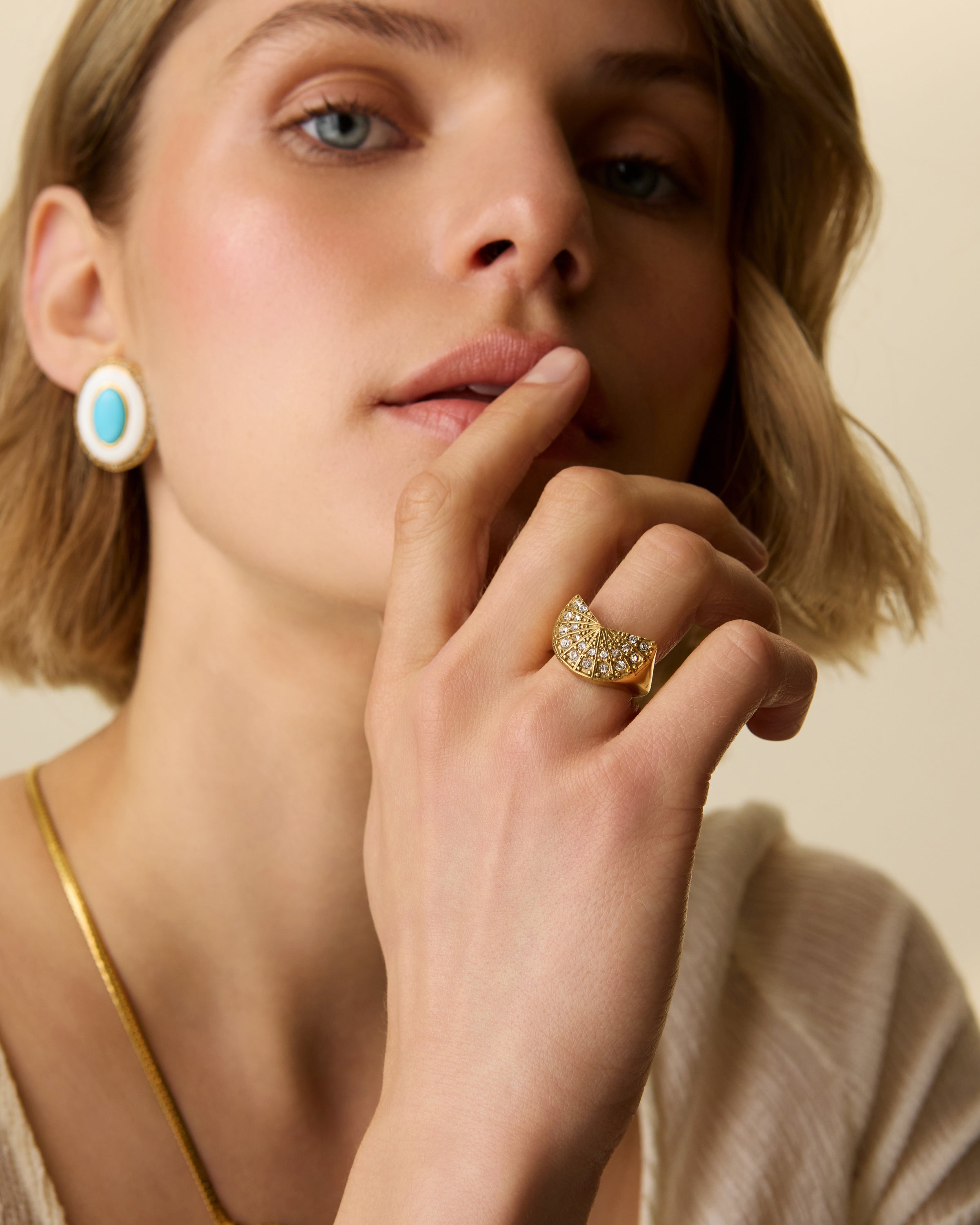 Close-up model shot of a model wearing These vintage-inspired oval earrings combine glossy turquoise and white enamel with a halo of sparkling crystals, all framed in warm gold-toned detailing. Effortlessly glamorous, they’re the perfect pop of colour to elevate summer dressing — from sundresses to silky evening looks.