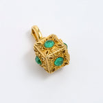 A gold cube charm featuring green emerald-cut gemstones on each side, on a white background.