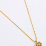 A gold chain necklace with a small cube pendant featuring green gemstone accents, displayed on a white background.
