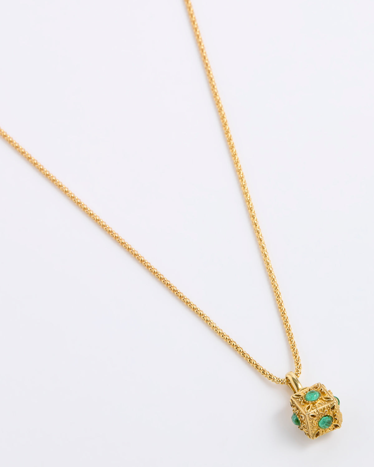 A gold chain necklace with a small cube pendant featuring green gemstone accents, displayed on a white background.
