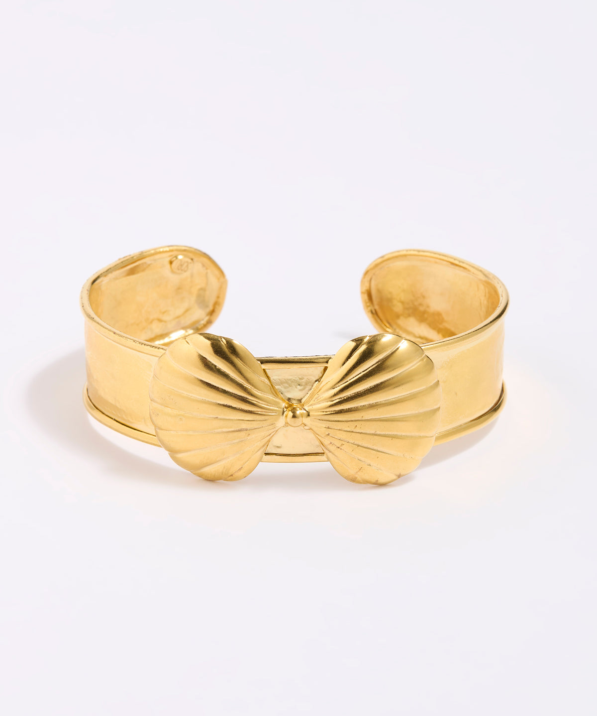 Gold coloured shell-shaped cuff bracelet on a light gray background