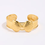 Gold coloured shell-shaped cuff bracelet on a light gray background