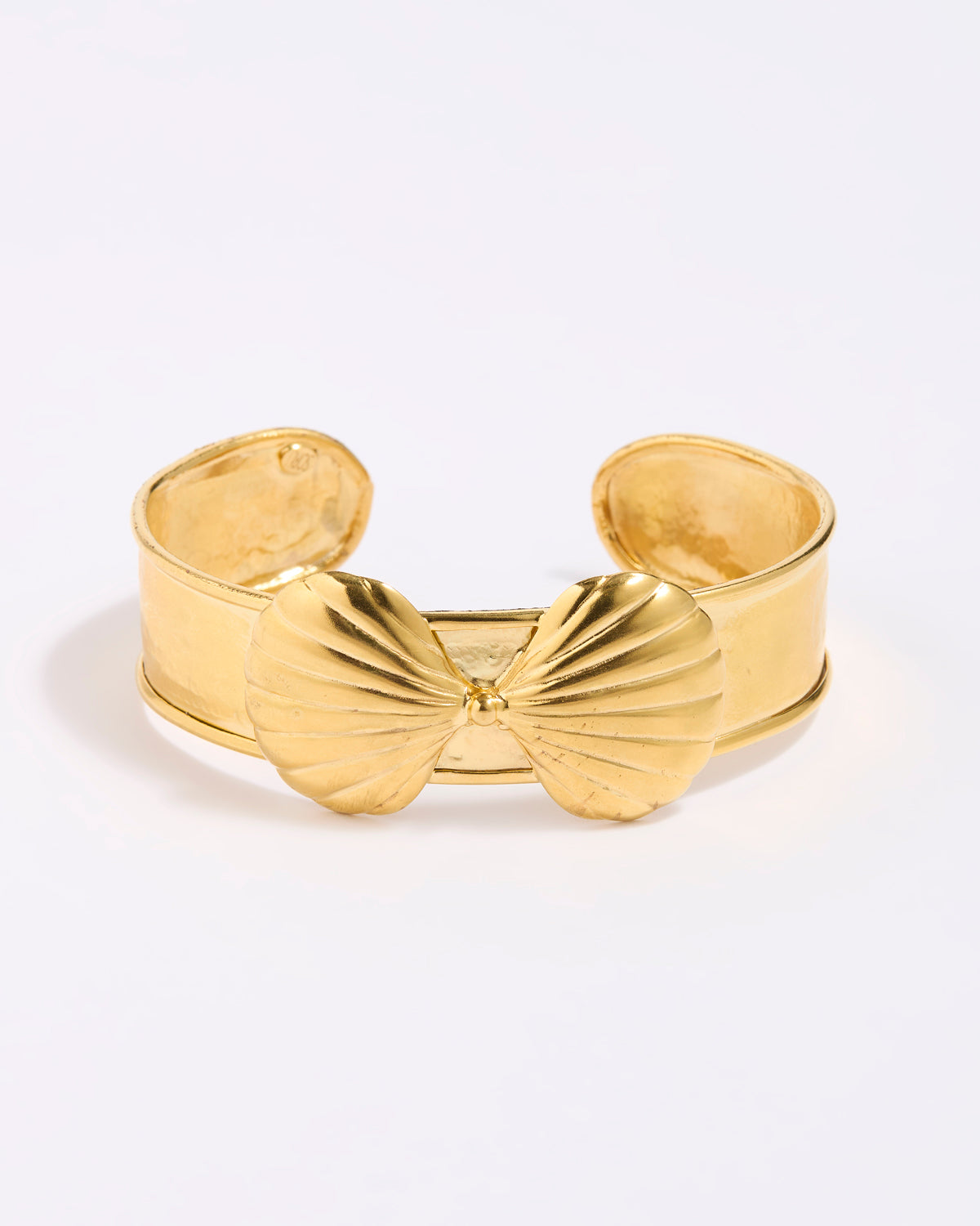 Gold coloured shell-shaped cuff bracelet on a light gray background