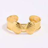 Gold coloured shell-shaped cuff bracelet on a light gray background