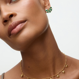 Close-up of a woman wearing a gold star necklace and malachite pearl fan earrings on a neutral background