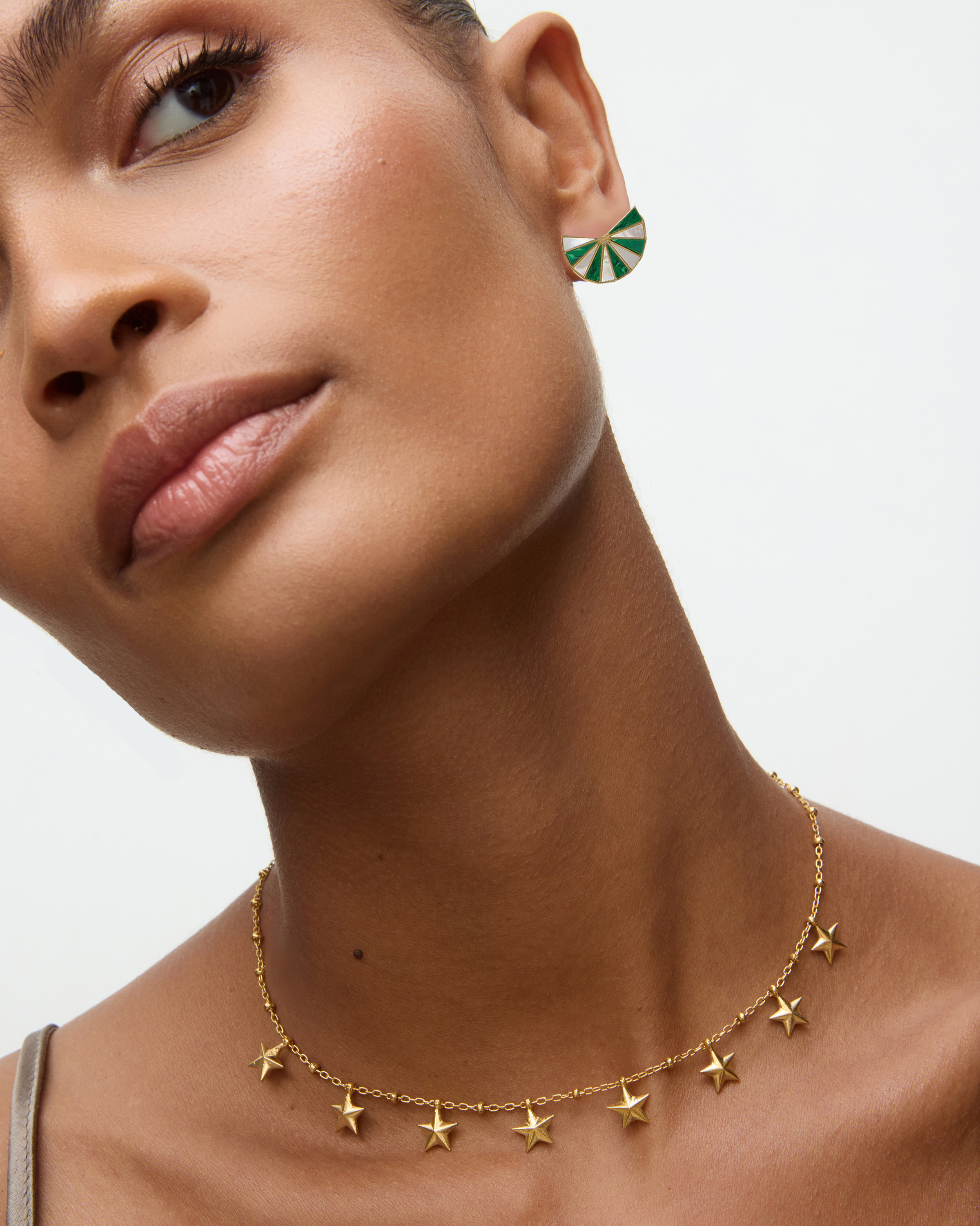 Close-up of a woman wearing a gold star necklace and malachite pearl fan earrings on a neutral background