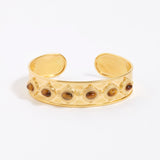Gold cuff bracelet with embedded stones on a white background