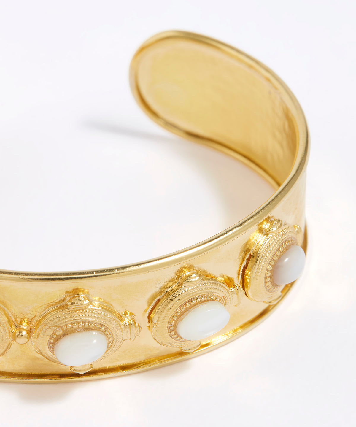 Close up image of Gold cuff with intricate design and 6 small oval mother of pearls shown on a white background