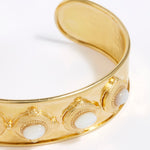 Close up image of Gold cuff with intricate design and 6 small oval mother of pearls shown on a white background