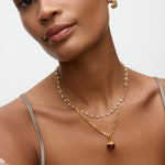 gold necklace with a brown glass pendant on a neutral background