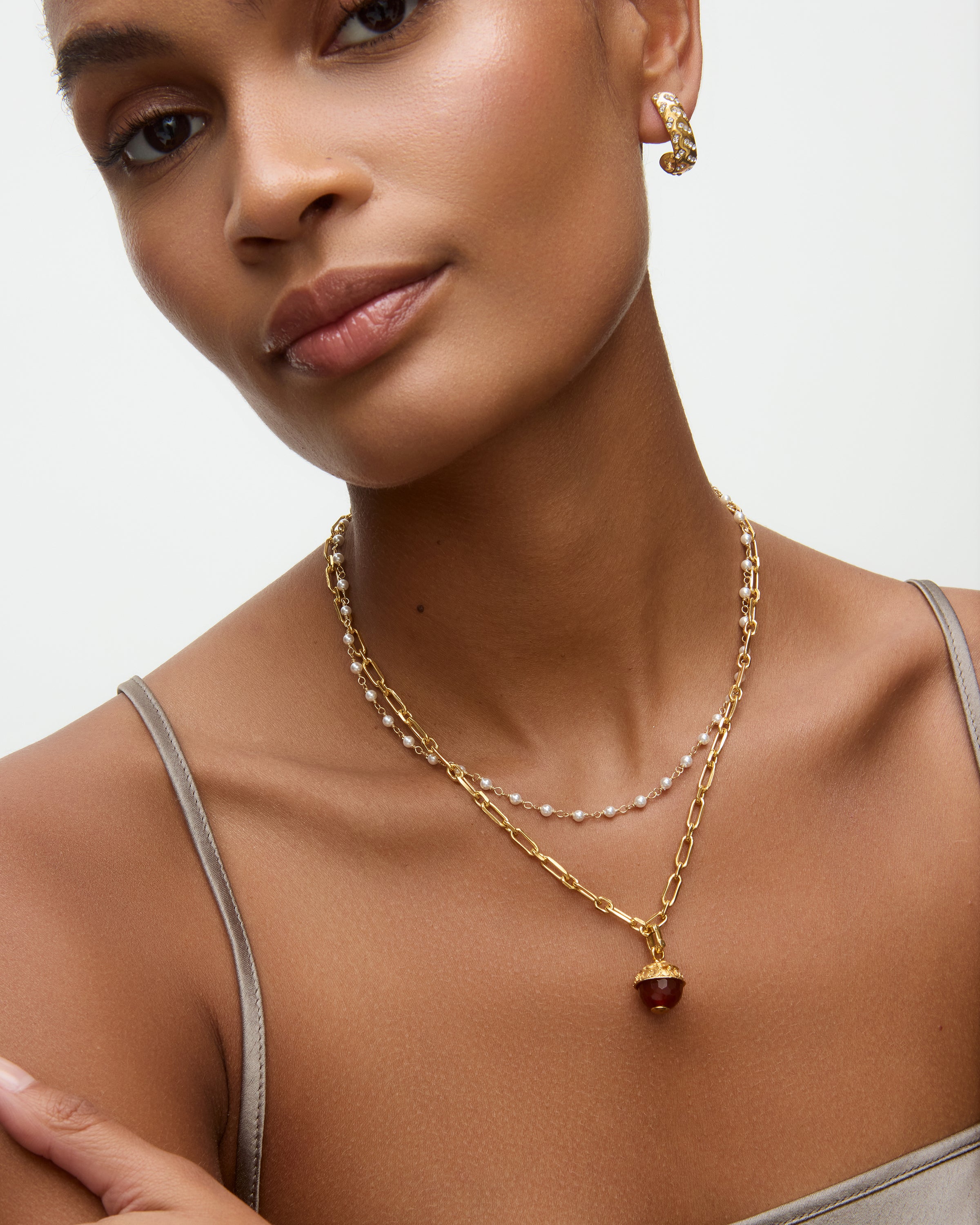 gold necklace with a brown glass pendant on a neutral background