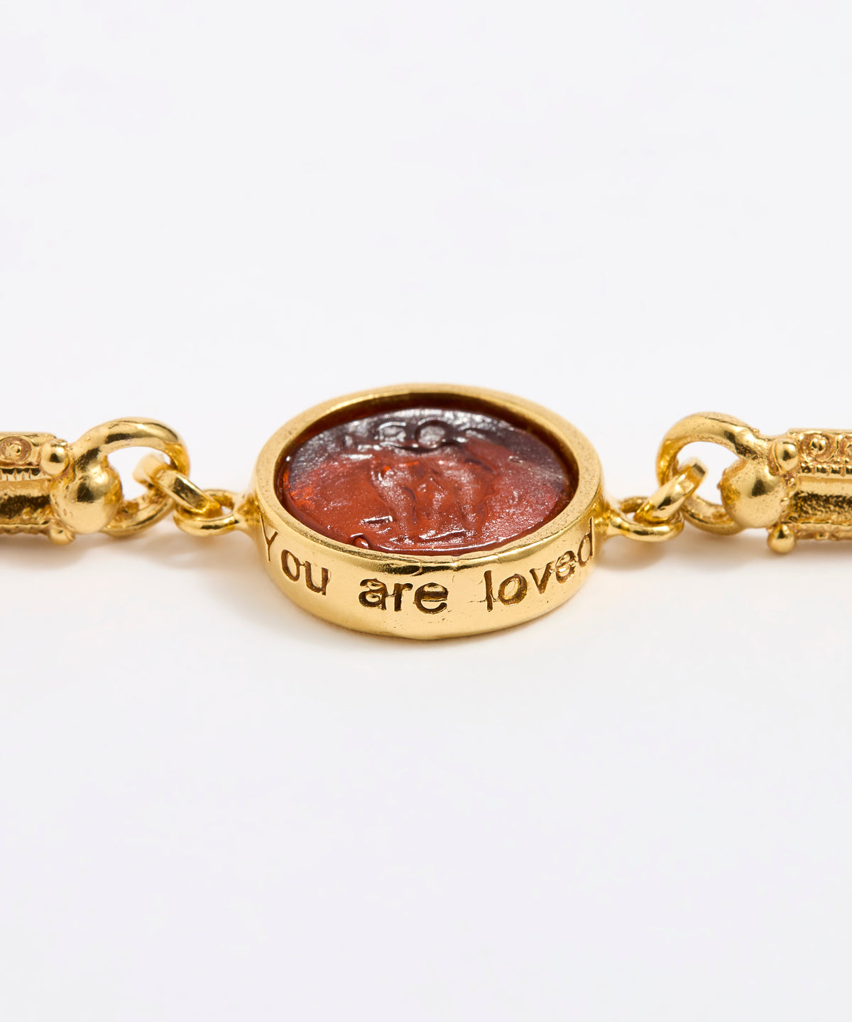 Close up of Gold link bracelet with round pendant in the centre with topaz glass and inscription ' you are loved' 