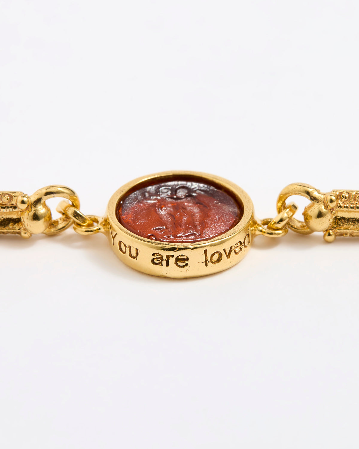 Close up of Gold link bracelet with round pendant in the centre with topaz glass and inscription ' you are loved' 