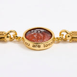Close up of Gold link bracelet with round pendant in the centre with topaz glass and inscription ' you are loved' 