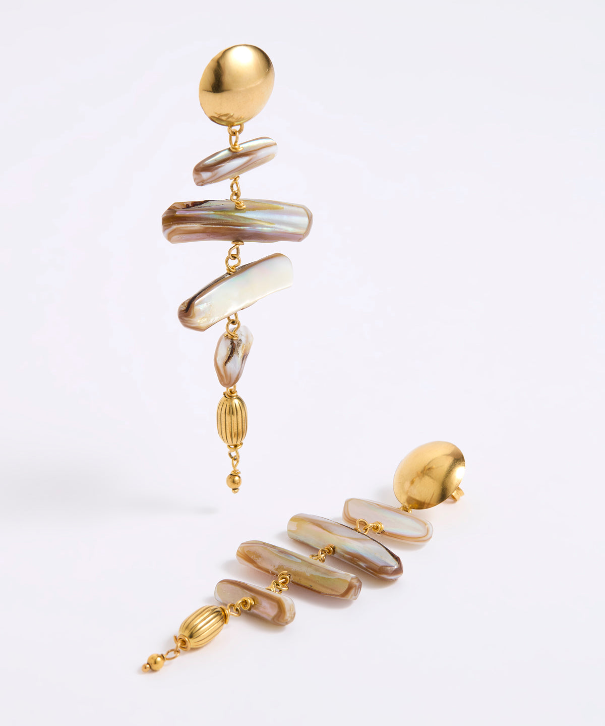 A pair of gold-toned statement dangle earrings with irregular iridescent shell-like discs in cream, beige, and brown tones, photographed on a clean white studio background.