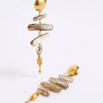 A pair of gold-toned statement dangle earrings with irregular iridescent shell-like discs in cream, beige, and brown tones, photographed on a clean white studio background.