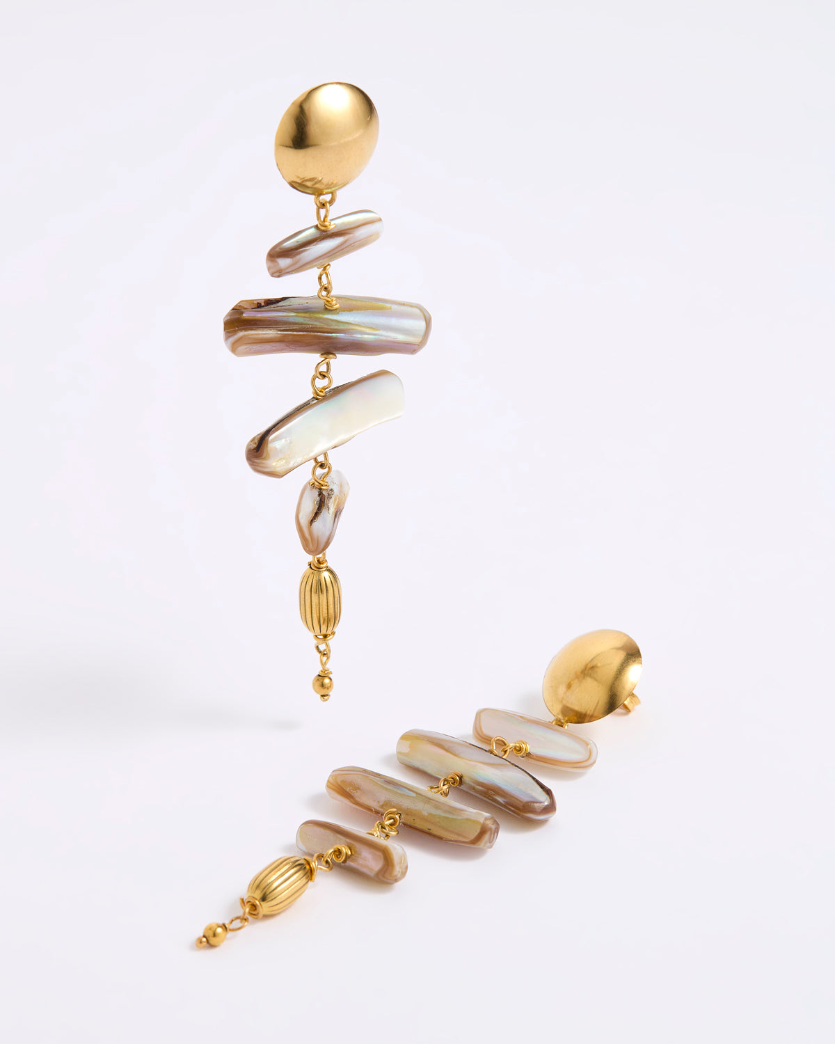A pair of gold-toned statement dangle earrings with irregular iridescent shell-like discs in cream, beige, and brown tones, photographed on a clean white studio background.