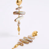 A pair of gold-toned statement dangle earrings with irregular iridescent shell-like discs in cream, beige, and brown tones, photographed on a clean white studio background.