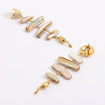 A pair of gold-tone drop earrings featuring irregular, polished shell-like segments in cream, beige, and white, accented with small gold beads, shown on a clean white background.
