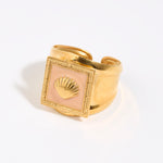 Gold ring with a shell design within peach coloured enamel square setting,  on a light background