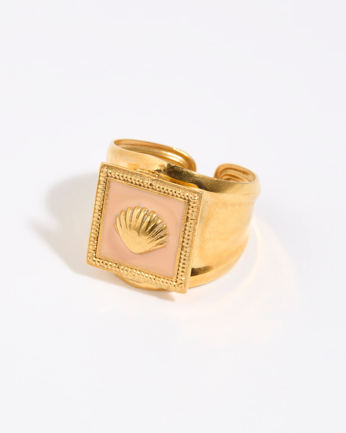 Gold ring with a shell design within peach coloured enamel square setting,  on a light background