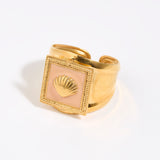Gold ring with a shell design within peach coloured enamel square setting,  on a light background