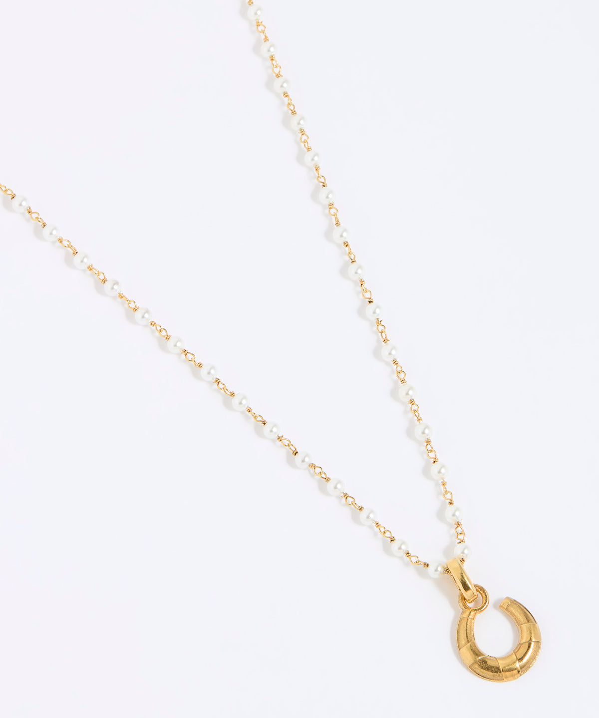 Gold coloured and pearl necklace with a small horseshoe pendant on a white background