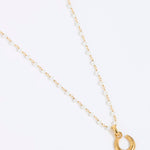 Gold coloured and pearl necklace with a small horseshoe pendant on a white background